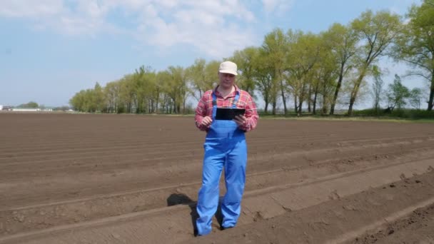 Boer, agronomist staat tussen bodemrijen op het landbouwveld, het testen van de kwaliteit van aardappel planten door cultivator. moderne landbouw. zonnige lentedag. — Stockvideo