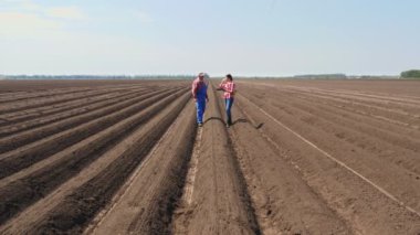 Çiftçi ve tarımcı, tarladaki toprak sıraları arasında, tabletle, ekicinin patates ekme kalitesini test ederek derin bir çizgide yürüyor. Modern tarım. Bahar güneşli gün.