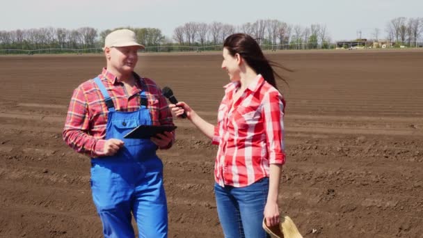 Journalisten intervjuar bonden för TV-nyhetssändning om Modern Jordbruksodling. bakgrund till den nyplöjda jordbruksarealen. — Stockvideo