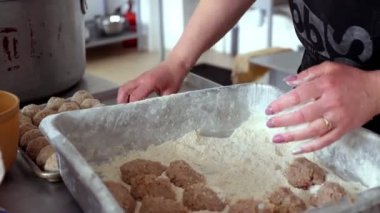 Yakın plan, bir kadın aşçı köfte pişirir, un parçalarına kıyma batırır ve pişirme tepsisine yayar..