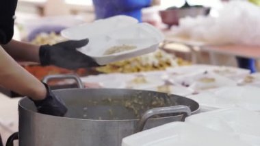 Yakın plan, kadın gönüllü lapayı büyük tavadan yemek kutusuna koyar. Yoksul ve evsizler için sıcak yemek. Bedava yemek servisi. bağış yardımı,