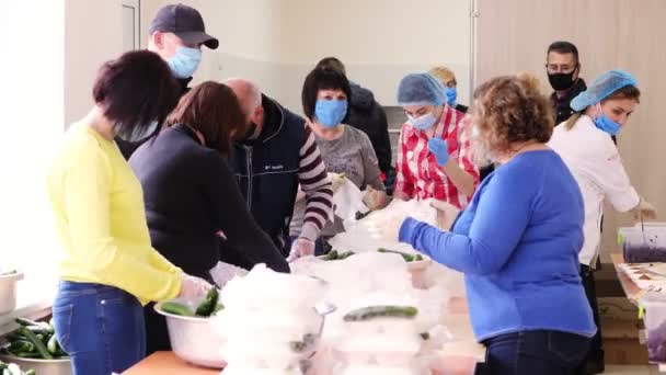 CHERKASY, UKRAINE, 18 mei 2020: vrijwilligers wikkelen lunchboxen met Liefdadigheidsmaaltijden in plastic zakken, voegen komkommers toe. gratis voedselverstrekking voor arme mensen tijdens het gezelschap19. Liefdadigheidsproject, steun verlenen — Stockvideo
