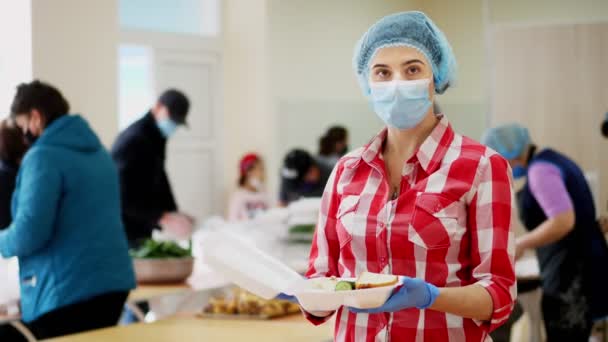 Vrouwelijke vrijwilliger in masker en handschoenen houdt in handen een schuim lunchbox met Charity warme maaltijd voor arme, daklozen tijdens het afsluiten van gezelschap19. Gratis levering van voedsel. donorsteun. — Stockvideo