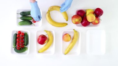 Üst Manzara. Koruyucu eldivenlerdeki gönüllüler bakkal paketleri, meyve ve sebzeleri tepsilere koyup kapatıyorlar. Coronavirus sırasında yemek servisi ve paket servisi. İnternetten alışveriş.