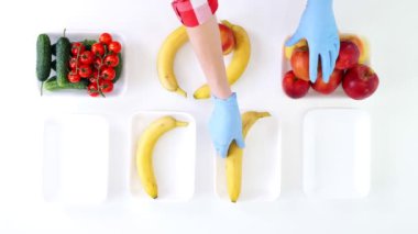 Üst Manzara. Koruyucu eldivenlerdeki gönüllüler bakkal paketleri, meyve ve sebzeleri tepsilere koyup kapatıyorlar. Coronavirus sırasında yemek servisi ve paket servisi. İnternetten alışveriş.