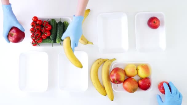 Вид зверху. Волонтер в захисних рукавичках пакує продукти харчування, кладе фрукти та овочі в лотки, крупним планом. Служба доставки продуктів харчування під час коронавірусу. Шопінг онлайн . — стокове відео