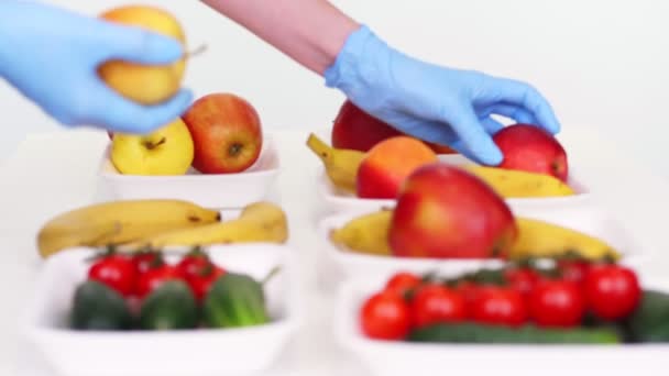 Volontär i skyddshandskar förpackningar livsmedel, sätter frukt och grönsaker i brickor, närbild. Matleverans med takeaway och dörr, under coronavirus. Handla online. — Stockvideo