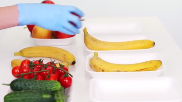 Koruyucu eldivenlerdeki gönüllüler bakkal paketleri, meyve ve sebzeleri tepsilere koyup kapatıyorlar. Coronavirus sırasında yemek servisi ve paket servisi. İnternetten alışveriş. — Stok video