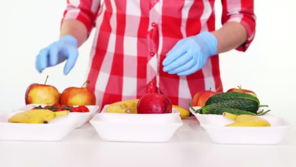 Volontär i skyddshandskar förpackningar livsmedel, sätter frukt och grönsaker i brickor, närbild. Matleverans med takeaway och dörr, under coronavirus. Handla online. — Stockvideo