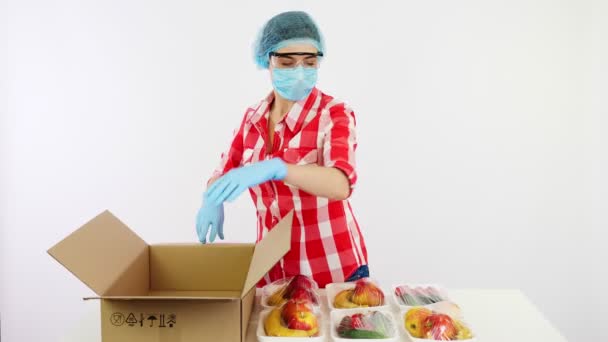 Voluntário em luvas de proteção e máscara embala supermercado, frutas, legumes em caixa de papelão. Takeaway, serviço de entrega de comida porta, durante o coronavírus. Compras online. Caridade . — Vídeo de Stock