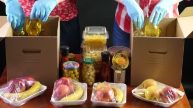 Yakın plan, koruyucu eldivenli gönüllüler marketi karton bağış kutularına dolduruyorlar. Coronavirus sırasında paket servis, kapı yemek servisi. İnternetten alışveriş. Hayırseverlik.