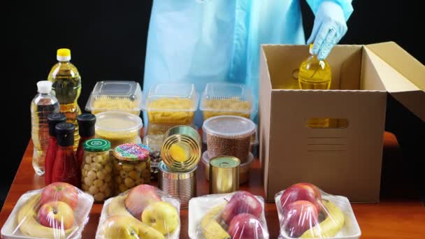 Close-up, Voluntario en traje de protección, guantes paquetes de comestibles a cartón caja de donación. Despegue, servicio de entrega de comida a domicilio, durante coronavirus. Compras en línea. Caridad . — Vídeos de Stock