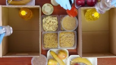 Üst düzey, yakın plan, koruyucu eldivenli gönüllüler marketi karton bağış kutularına dolduruyor. Coronavirus sırasında paket servis, kapı yemek servisi. İnternetten alışveriş. Hayırseverlik.