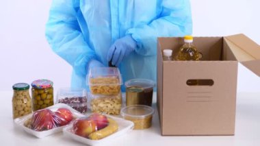 Koruyucu eldivenler içinde gönüllü, market alışverişini karton bağış kutusuna paketliyor. Coronavirus sırasında paket servis, kapı yemek servisi. İnternetten alışveriş. Hayırseverlik.