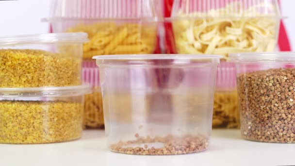 Primer plano, el trigo sarraceno se vierte en envases de plástico. fondo de las mismas cajas de plástico con pasta y cereales . — Vídeos de Stock