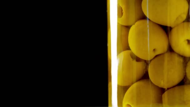 Close-up, τουρσί μεγάλες πράσινες ελιές σε ένα γυάλινο βάζο, το προϊόν τροφίμων περιστρέφεται σε μαύρο φόντο. παντοπωλείο online ψώνια. παράδοση τροφίμων, συντήρηση τροφίμων — Αρχείο Βίντεο