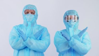 Doktor ve hemşire, özel koruyucu giysiler, üniformalar, maskeler, gözlükler içinde kameraya bakıyor, el hareketlerini gösteriyor. Koronavirüs salgını. Beyaz arka plan. Coronavirus koruması