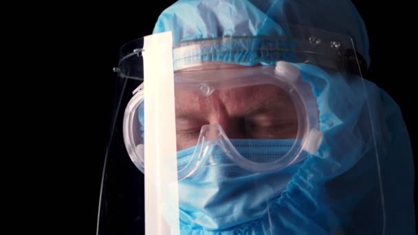 Erkek bir sağlık çalışanının portresi. Yorgun ve yorgun doktor koronavirüs koruyucu üniforma, maske, gözlük ve koruyucu ekran çıkarıyor. Bir salgın covid-19 — Stok video