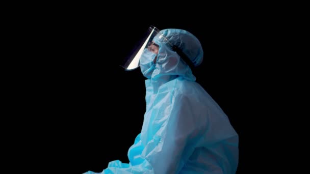 Vyčerpaný a unavený Ženský lékař nebo zdravotní sestra v ochranné uniformě, masce, brýlích a ochranné cloně sedí ve tmě na podlaze. Ohnisko Coronavirus Covid-19. — Stock video