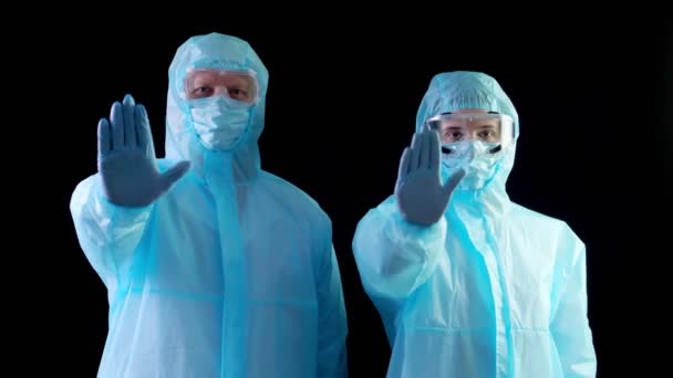 Doctor, nurse in special protective suits, masks, goggles, looking at camera, showing stop sign by palms, hands. coronavirus epidemic. black background. protection — Stock Video