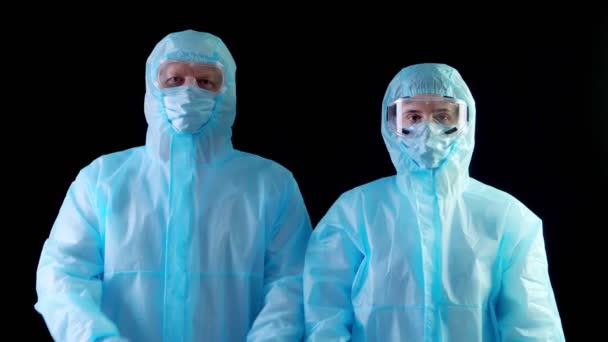 Doctor, nurse, in protective uniforms, masks, goggles, looking at camera, showing stop gesture by hands. coronavirus epidemic. black background. — Stock Video