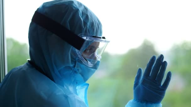 Medisch medewerker in een speciaal beschermend pak. vermoeide en uitgeputte arts leunde tegen het raam. Coronavirus epidemie, covid-19 uitbraak. bescherming — Stockvideo