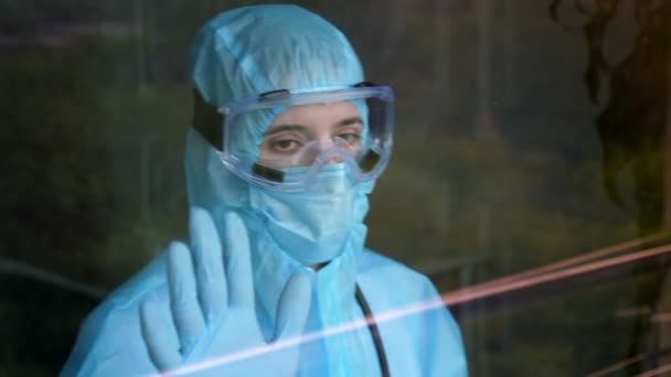 Medisch medewerker in een speciaal beschermend pak. vermoeide en uitgeputte arts leunde tegen het raam. Coronavirus epidemie, covid-19 uitbraak. bescherming — Stockvideo