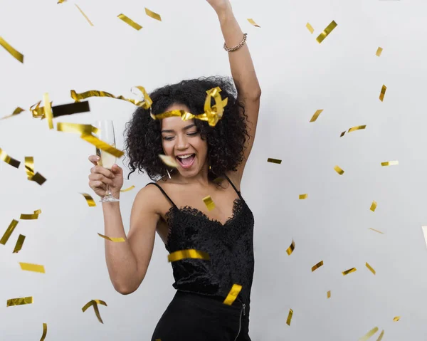 Happy woman dancing under confetti with glass of champagne at party