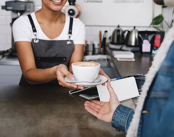 Unrecognizable coffee shop owner handing over a cup of coffee to her customer