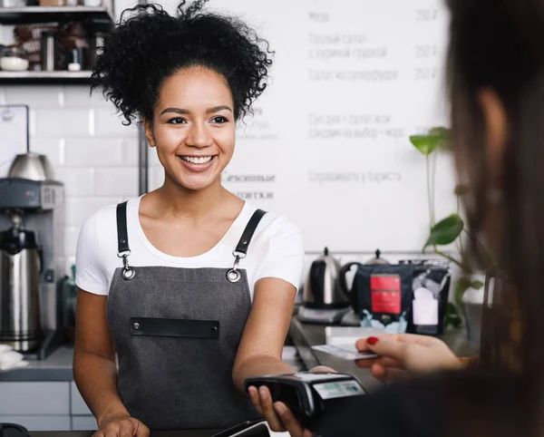 Smiling cashier accepting payment over nfc technology, looking on a buyer