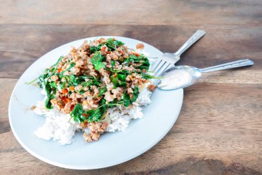 Üzerine kızarmış domuz eti ve fesleğenle birlikte beyaz bir tabakta pirinç. (Ön odak)