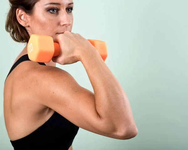 Turuncu bir dumbbell onun kol egzersiz için kullanan aktif genç kadın — Stok fotoğraf