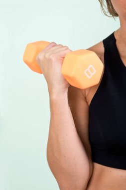 Onu kol egzersiz ev yapımı fitness salonunda spor salonu için turuncu bir dumbbell kullanan aktif genç kadın