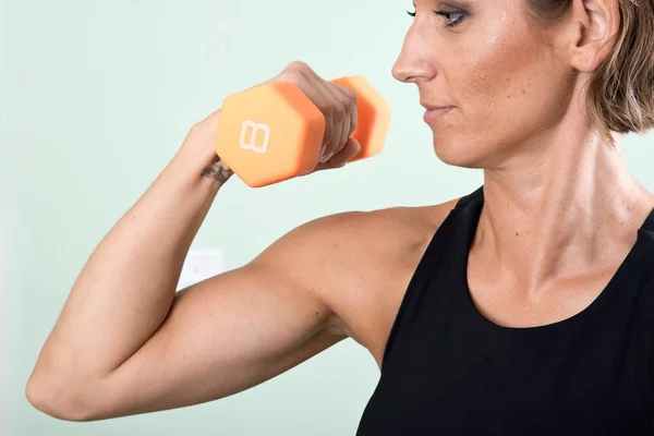 Onu kol egzersiz ev yapımı fitness salonunda spor salonu için turuncu bir dumbbell kullanan aktif genç kadın — Stok fotoğraf