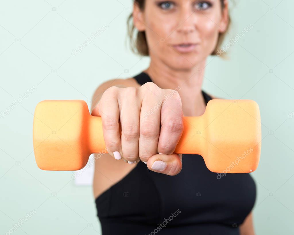Active young woman using a orange dumbbell for her arm exercise in homemade fitness gym studio