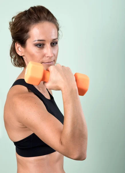 Onu kol egzersiz ev yapımı fitness salonunda spor salonu için turuncu bir dumbbell kullanan aktif genç kadın — Stok fotoğraf