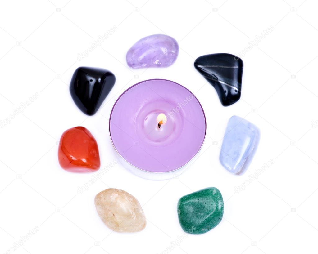 Lavender tea light candle surrounded by set of seven healing chakra stones for crystal healing, isolated on white background 