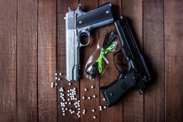 two pistols: a metallic and black are the glasses airsoft on a dark brown background