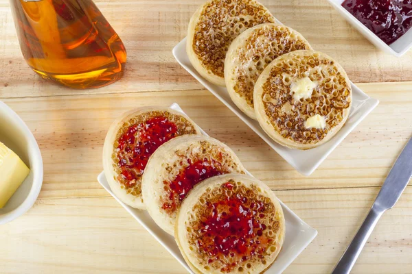 Freshly toasted crumpets with butter and jam on country table — Stockfoto