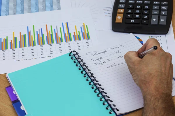 Acountant writing in his notebook and studying graphs — Stock Photo, Image
