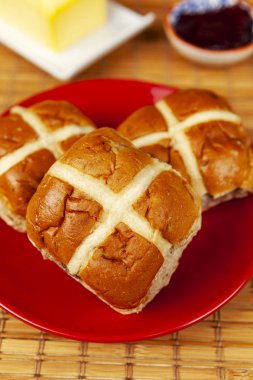 Three fresh hot cross buns on a red plate