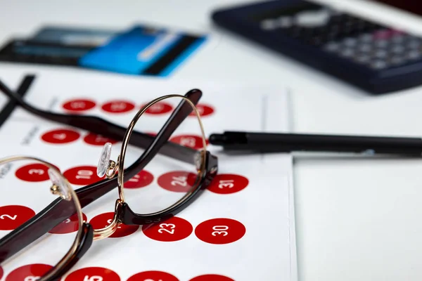 Pair of black rimmed spectacles laying on a calendar with some credit cards — 스톡 사진
