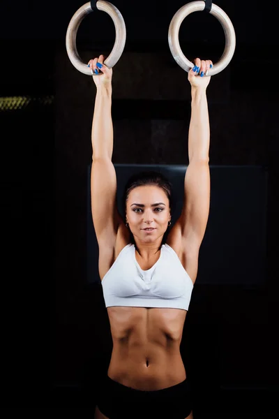 Crossfit. Porträt eines jungen, durchtrainierten, muskulösen Mädchens in weißem Top mit Gymnastikringen beim Training im Fitnessstudio. — Stockfoto