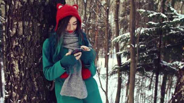 The friendly girl in the winter forest is typing a message on the phone. — Stock Video