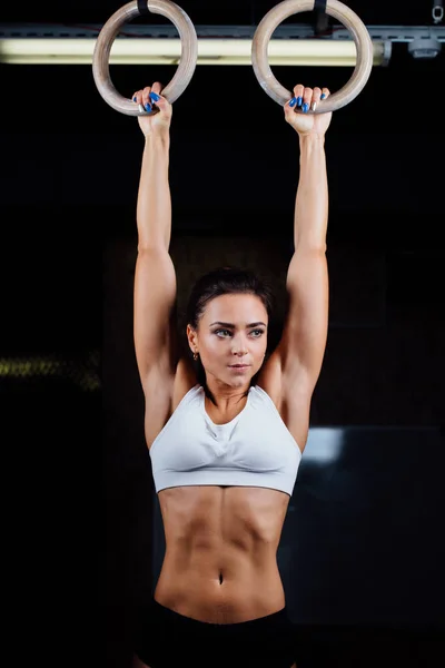 Portrait of young fit muscular girl in white top using gymnastic rings. — Stock Photo, Image