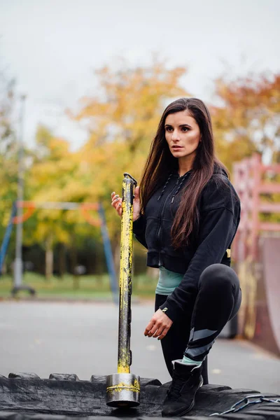 Menina posando no parque com martelo e pneu trator . — Fotografia de Stock