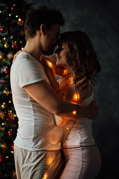 Casal em pijama no fundo da árvore de Natal — Fotografia de Stock