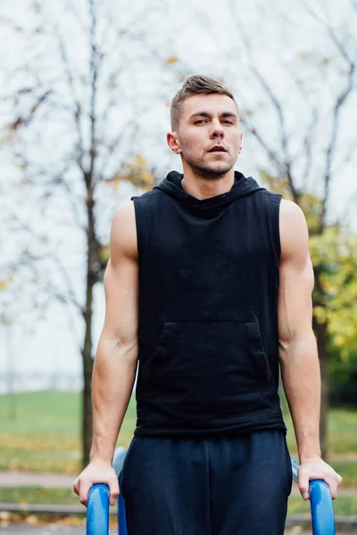 Portret koncentruje się mięśni młody mężczyzna w czarnym treningu ubrania robi spadki na poręczach. — Zdjęcie stockowe