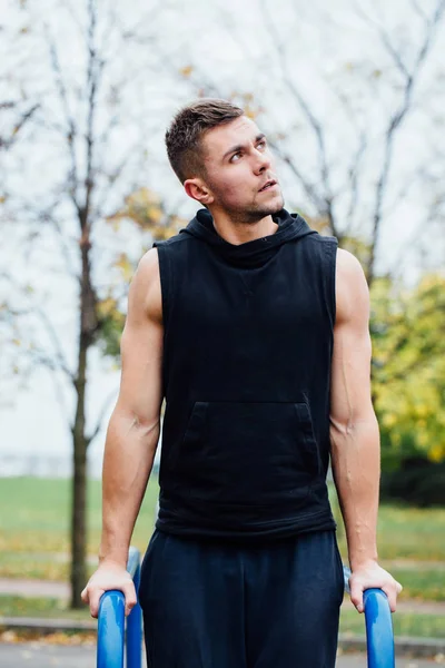 Portret koncentruje się mięśni młody mężczyzna w czarnym treningu ubrania robi spadki na poręczach. — Zdjęcie stockowe