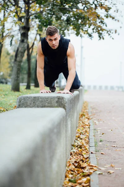 Robi ćwiczenia, trening w parku upadku męskiego runner. Push up z ławą. — Zdjęcie stockowe